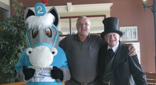 Grand River Raceway mascot Grandy with longtime guest Ray Rowarth and Greeter Tom Williams. For the past decade, Tom has greeted guests at the front door every race night | Iron Horse Photo